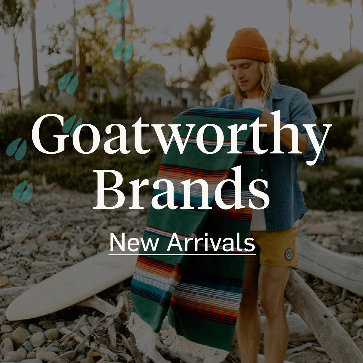 Goatworthy Brands New Arrivals — man in beanie holding colorful striped blanket on beach with driftwood and palm trees.