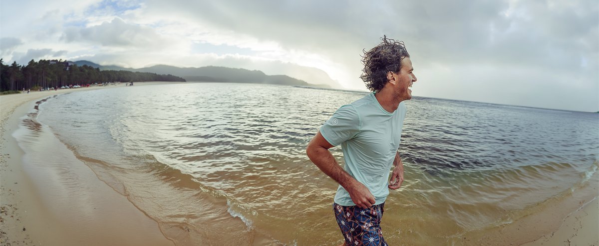 Man wearing Backcountry Tahoe pro LT shortsleeve shirt running through the waves on a beach.