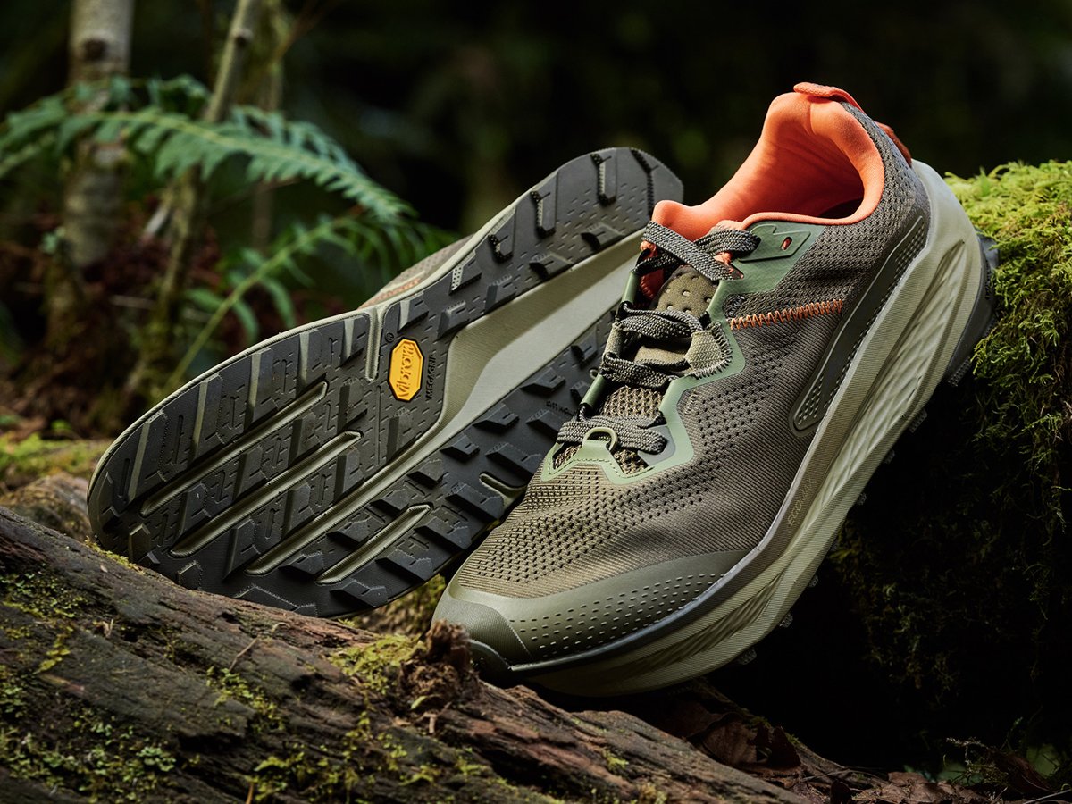 The New Altra Olympus 7 trail running shoe displayed on a mossy log in a forest setting.