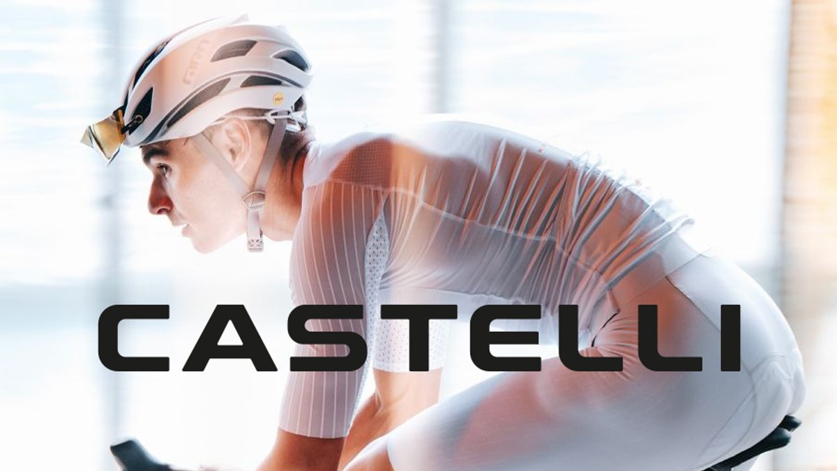 A close-up side profile of a focused cyclist in a white, aerodynamic Castelli jersey and helmet, leaning forward on a bike.