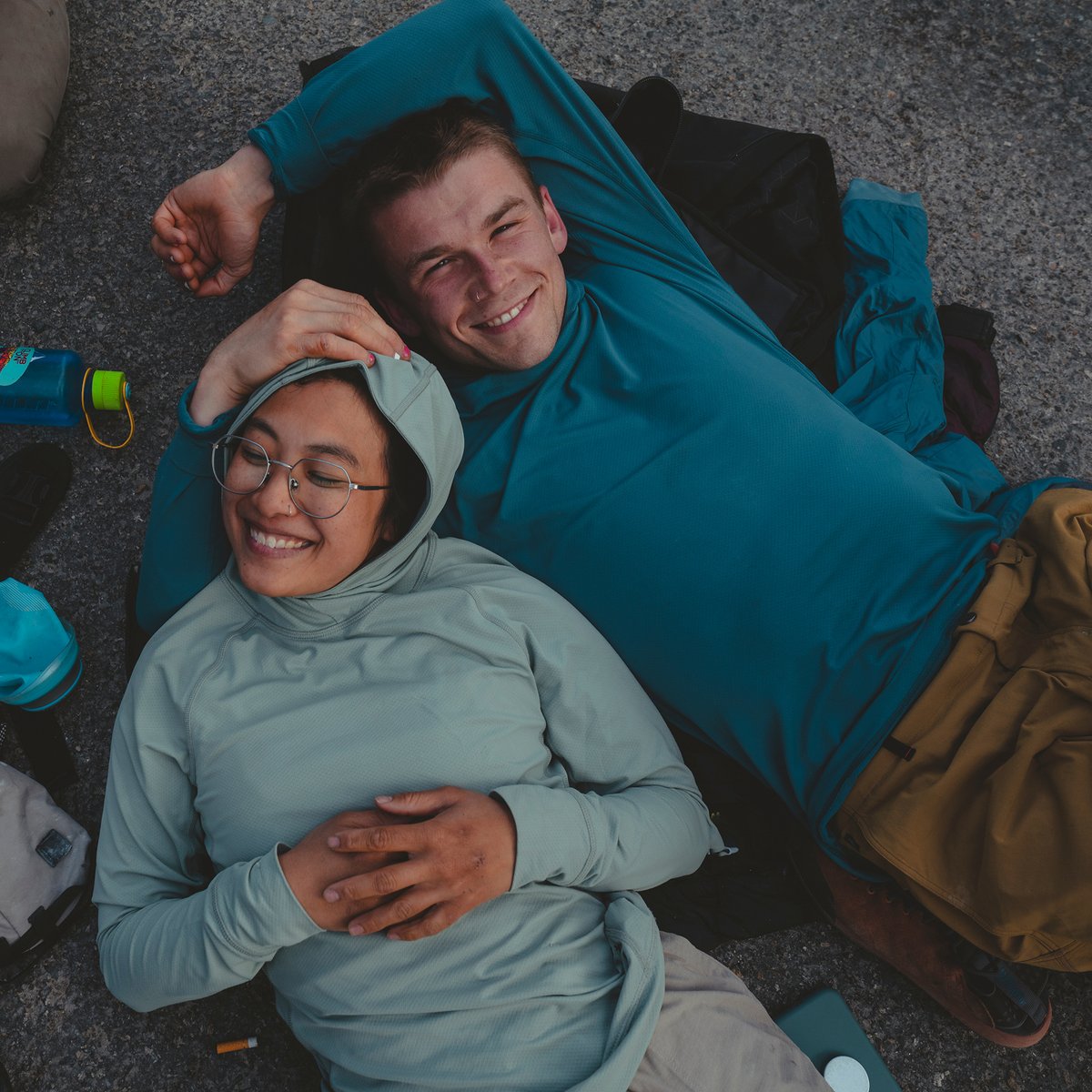 Two trad climbers wearing sun hoodies relax on a flat slab of granite.
