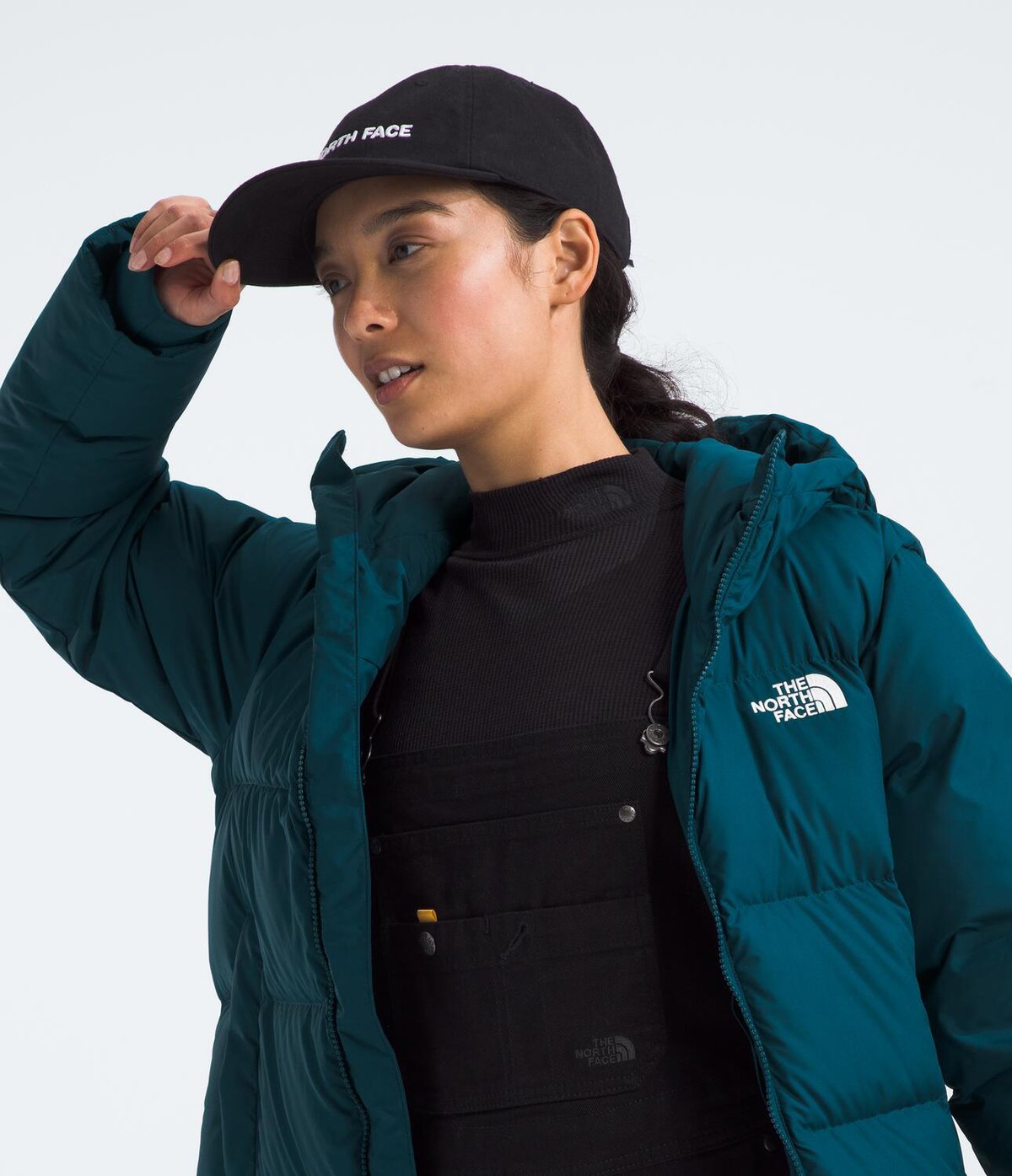A woman wearing a ballcap wears a Artic Down Parka unzipped