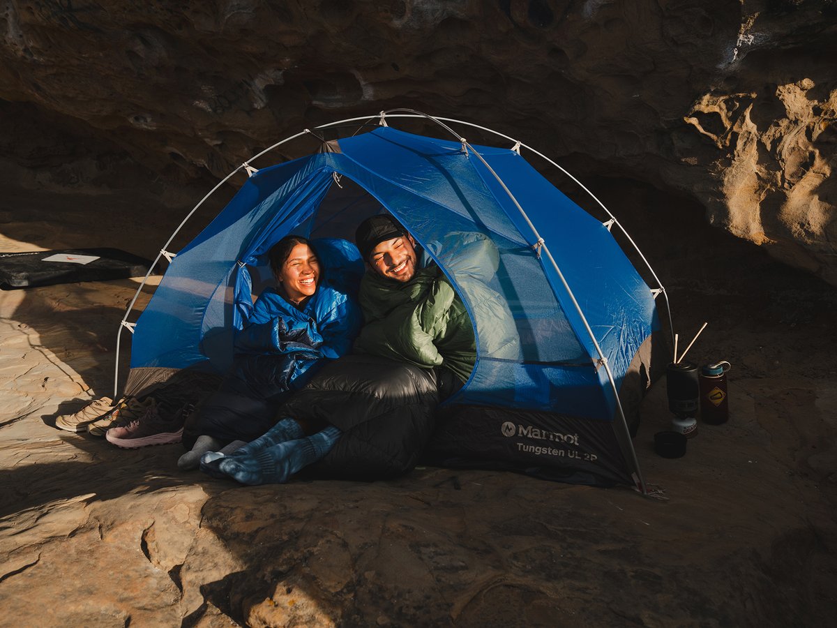 A of campers in sleeping bags, laying on their stomachs in a backpacking tent while smiling broadly. 