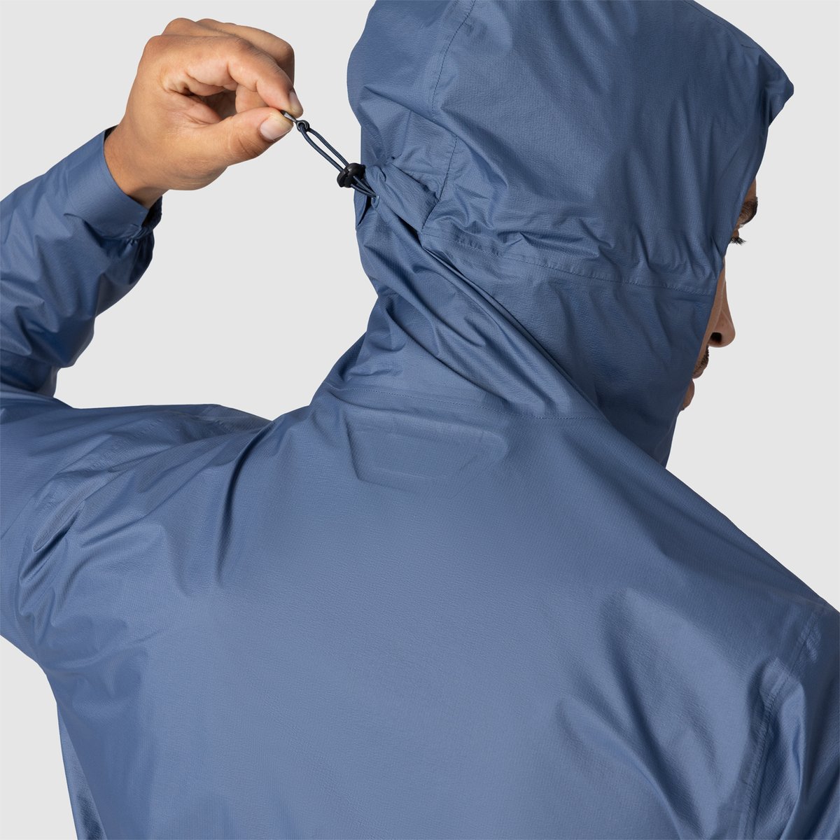 A person wears the Helium UL rain jacket, showcasing the cinch feature on the back of the hood