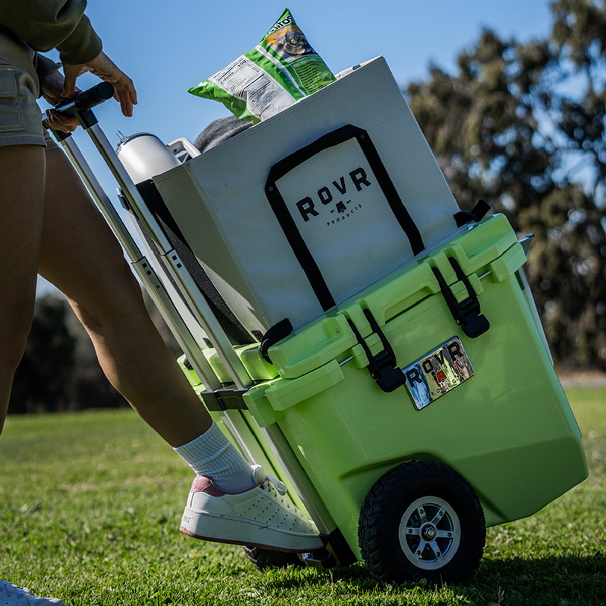 Person pulling the RovR RollR cooler across a grassy field using the telescoping handle, with gear stacked on top