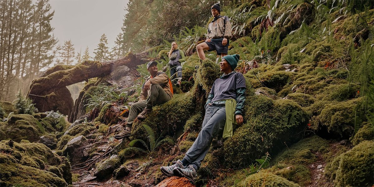Claude responded: Four hikers resting on a moss-covered rocky hillside in a misty Pacific Northwest forest, wearing layered outdoor apparel and hiking footwear.Four hikers resting on a moss-covered rocky hillside in a misty Pacific Northwest forest, wearing layered outdoor apparel and hiking footwear.