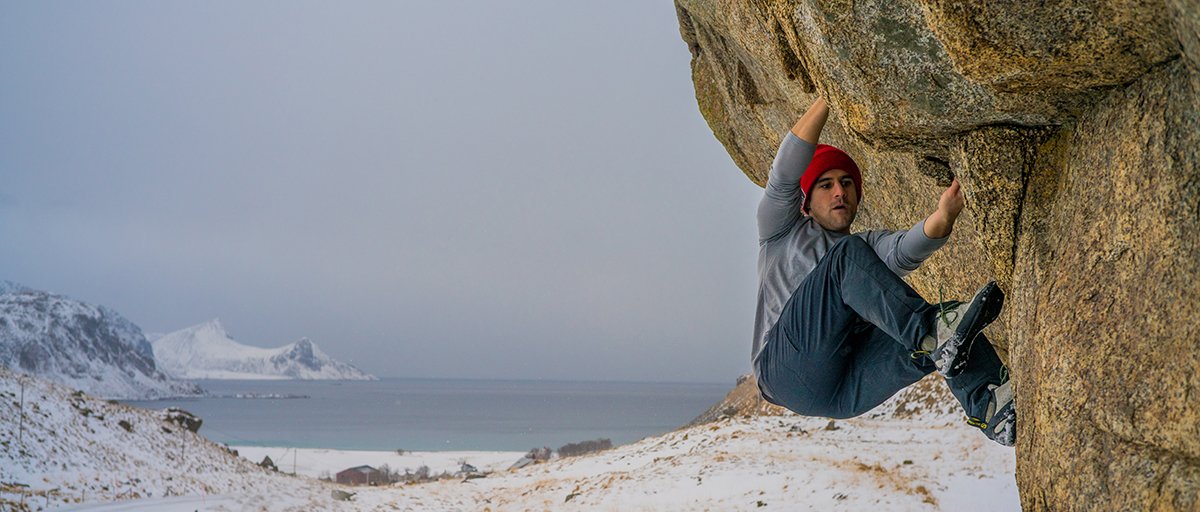 Male climber bouldering overhanging coastal granite rock with snowy fjord landscape in cold winter conditions