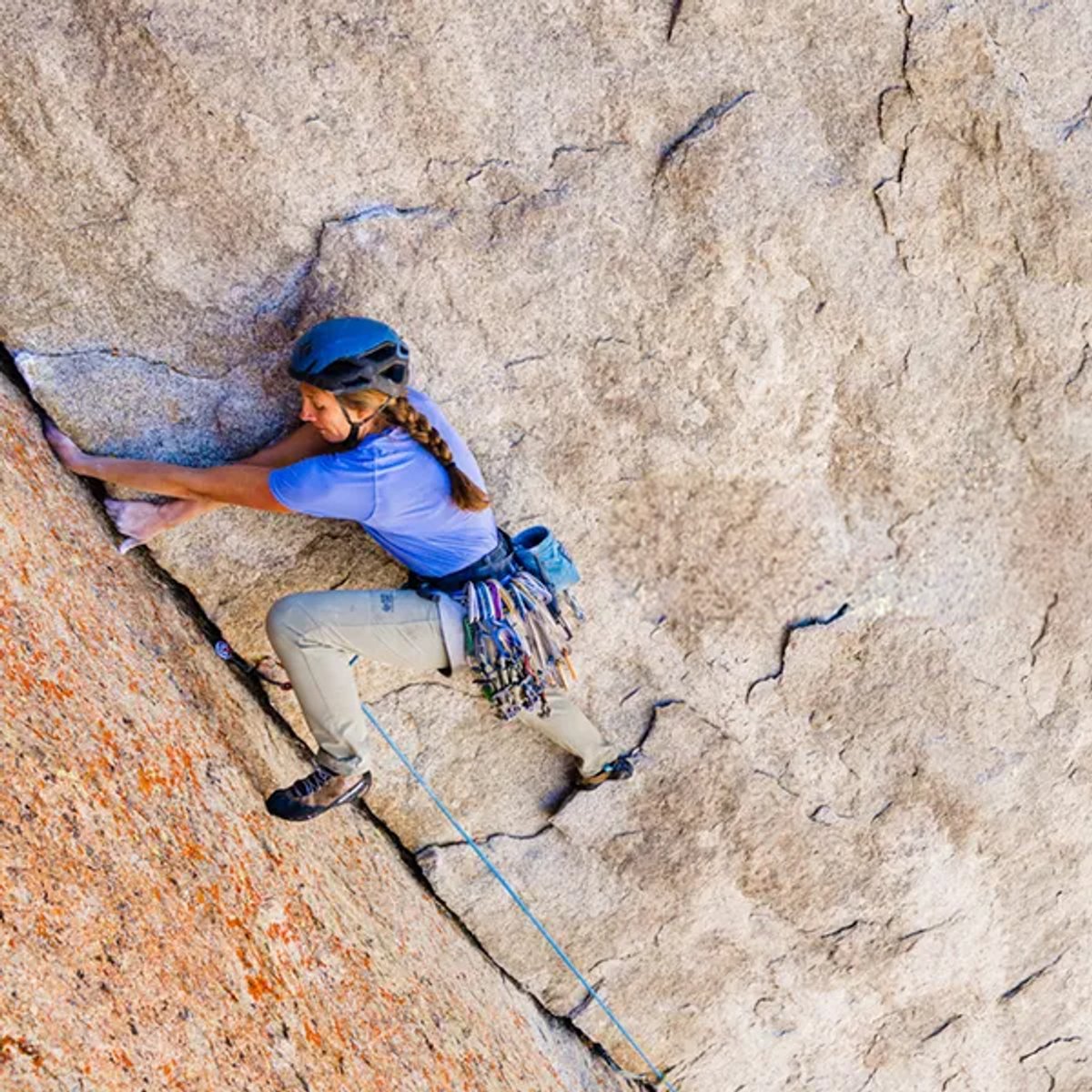 A woman climbs up a cliff face, wearing a Mountain Hardwear Crater Lake top. 