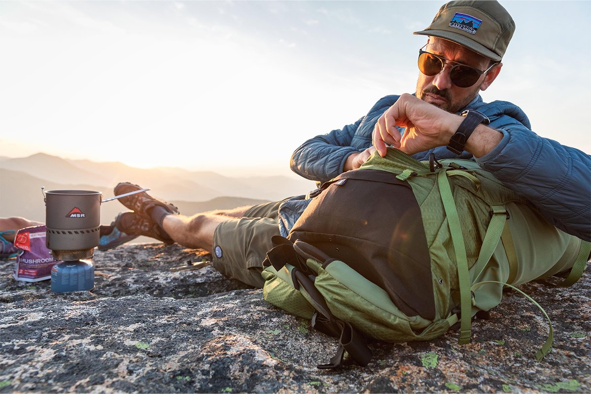A man sits on a rocky surface, reclining onto his Osprey backpack.