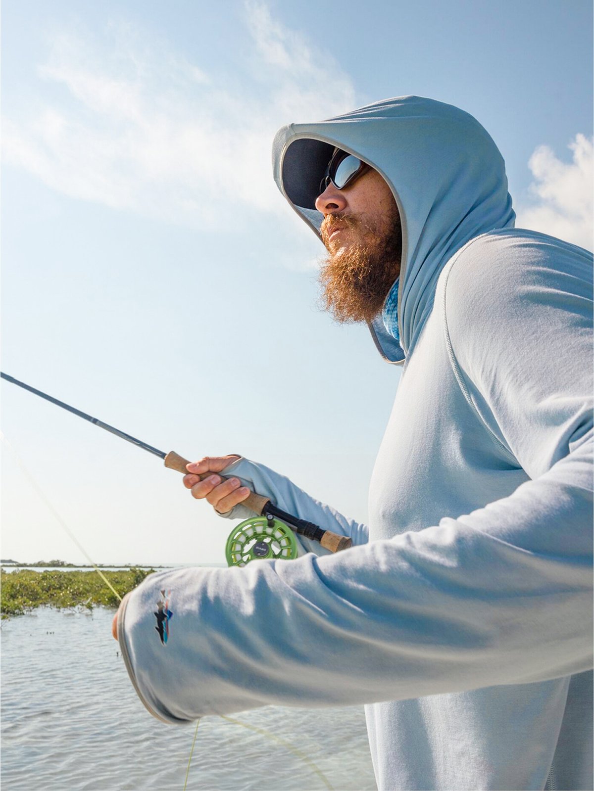 A bearded man wearing a sun hoodie is fly fishing.