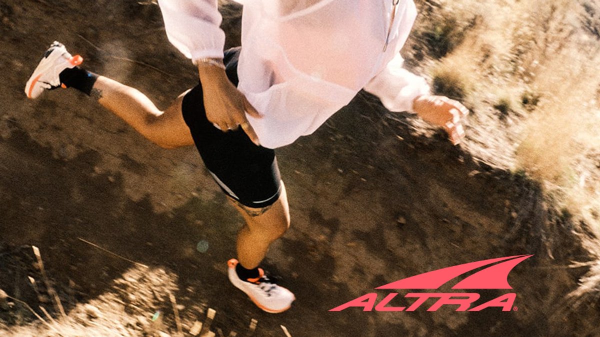 A runner in motion on a dirt trail wearing Altra running shoes, with the brand's coral logo in the corner.