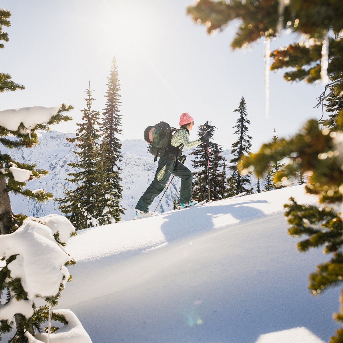 Wide shot of a snow-covered mountain ridge, layered clouds in the background, with person skinning uphill.