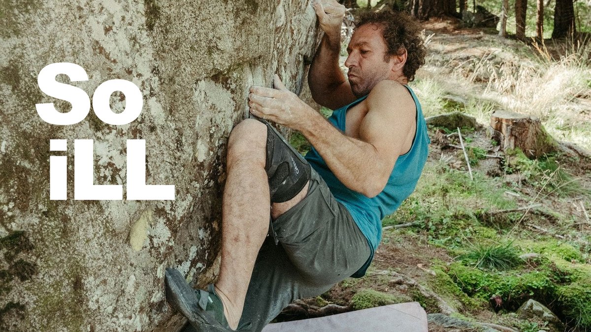 Man rock climbing on outdoor boulder in forest wearing blue tank top and gray shorts with "So Ill" text overlay.
