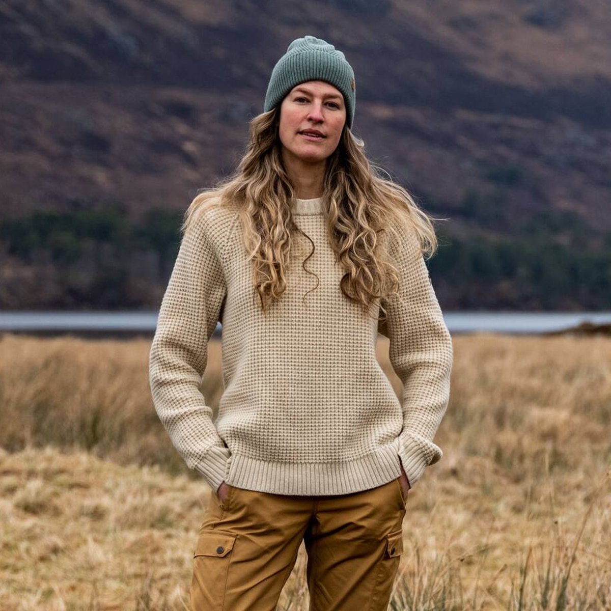 A woman standing in a field showing off her waffle kit sweater.