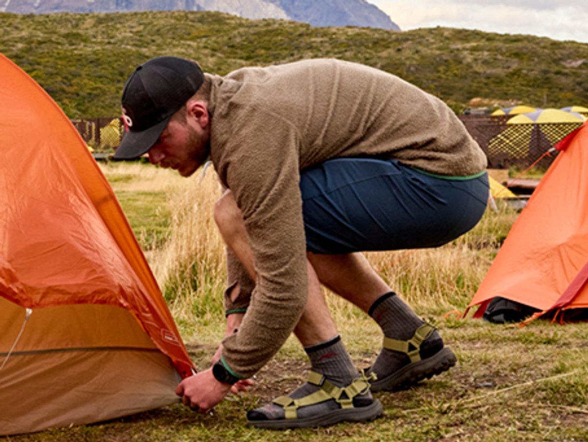 Person wearing fleece jacket steaking down a tent.