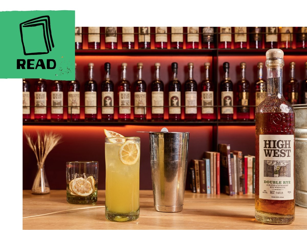 A bar countertop displays a tall cocktail garnished with dried lemon slices beside a bottle of High West Double Rye. A green flag includes an illustration of a book and the word “read.”