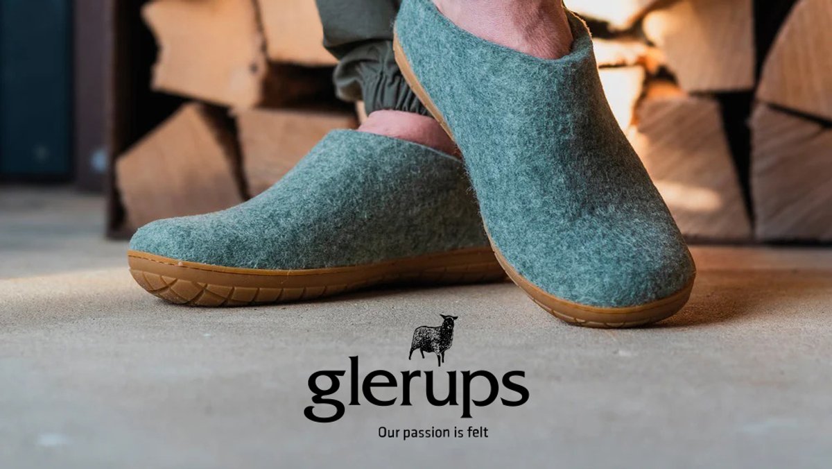 A person wearing teal wool felt Glerups slippers with natural rubber soles on a concrete floor, showcasing the brand's tagline "Our passion is felt."