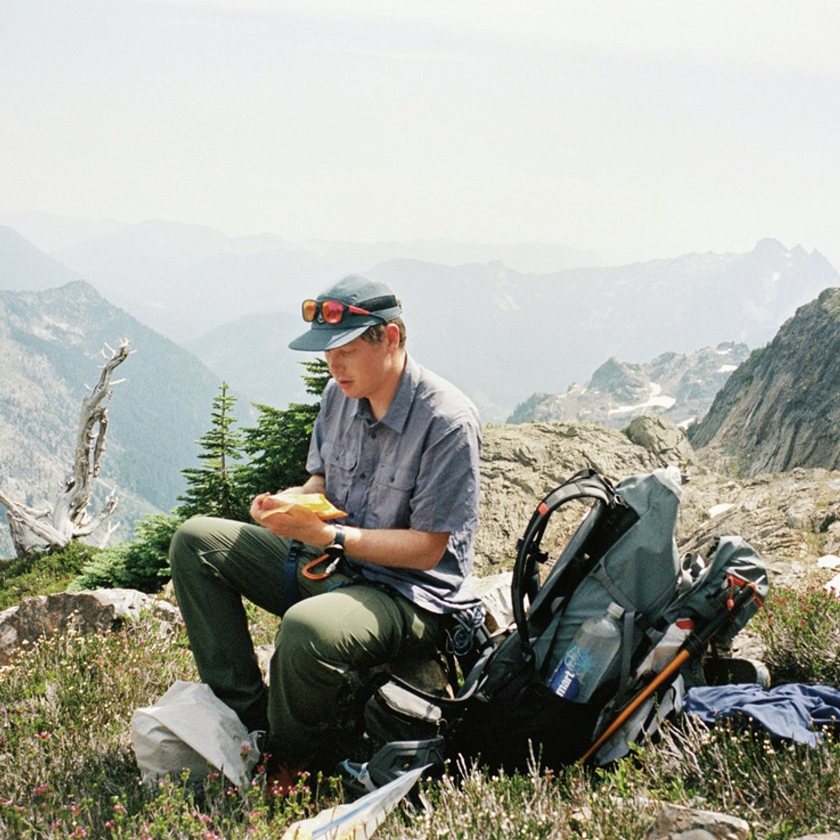 A man sits on a mountaintop, wearing a Canyon top.