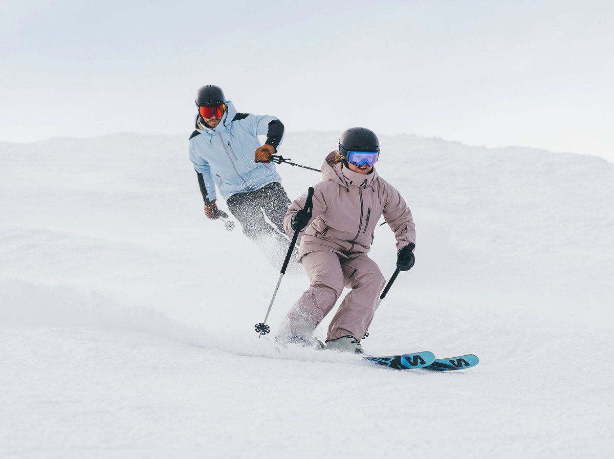 Two skiers carving through fresh snow. Summit+ Club limited time offer.