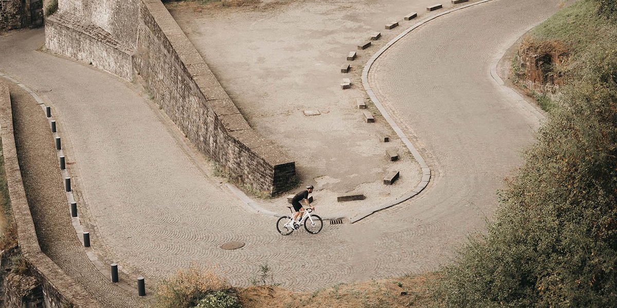Road cyclist riding up twisting hillside road.