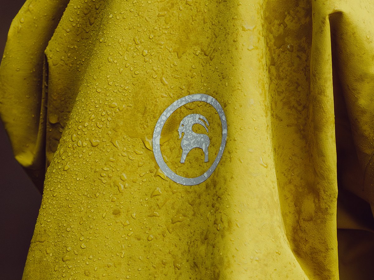 Water beading on yellow waterproof jacket chest with Backcountry goat logo visible through rain droplets