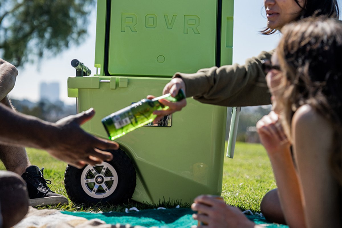 A group of adults on a blanket at a park, sharing drinks from the RovR RollR cooler.