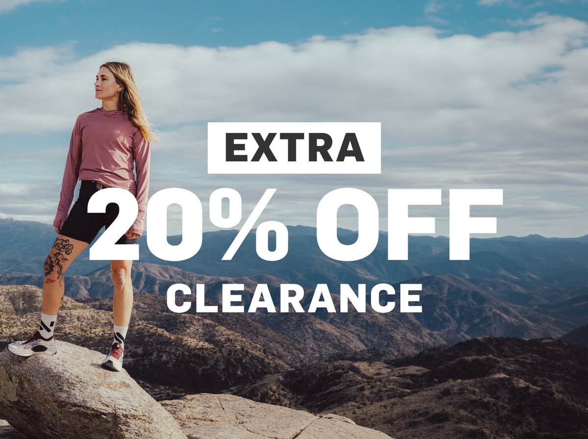 A woman stands on top of a mountain summit. Promotion text appears the left of her saying, “Extra 20% off clearance”. 