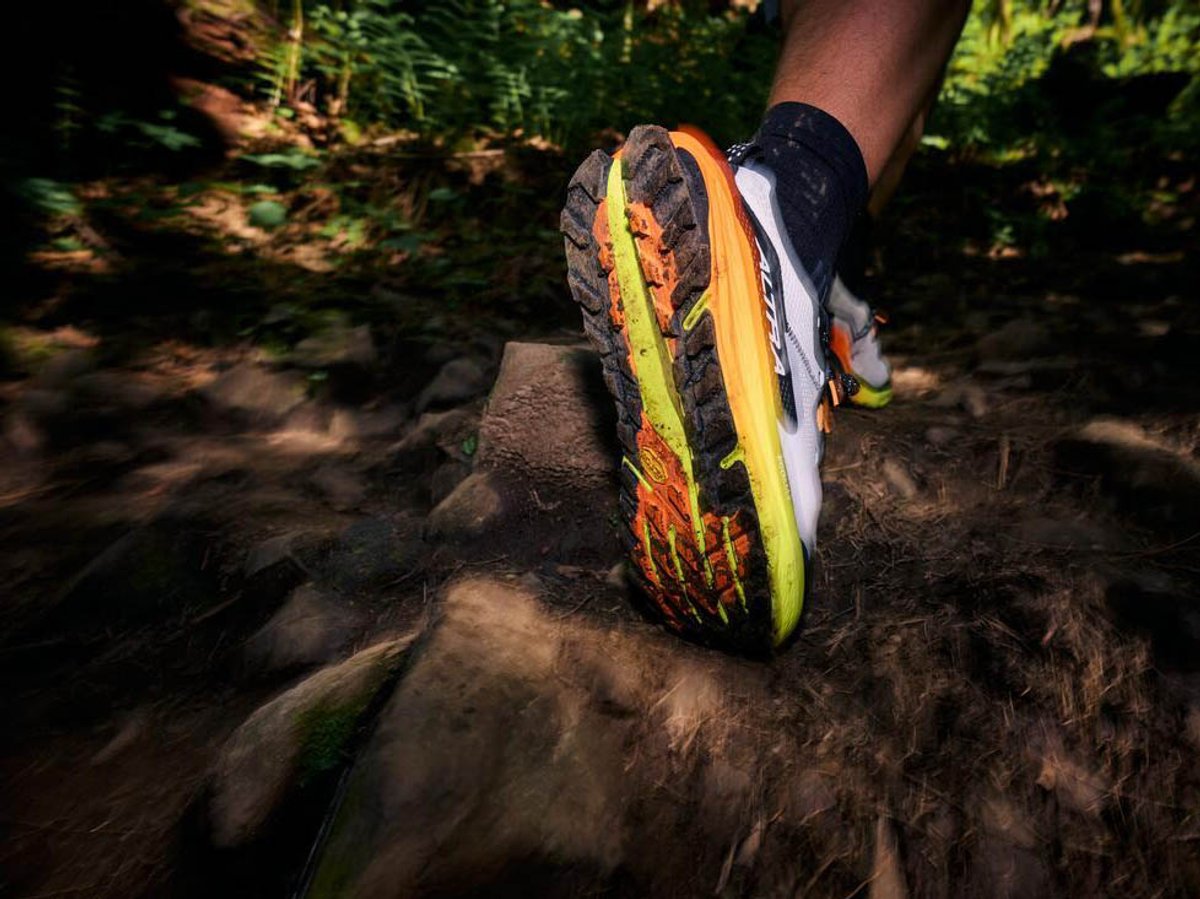 Close up of sole of muddy Altra trail shoe as runner runs away.