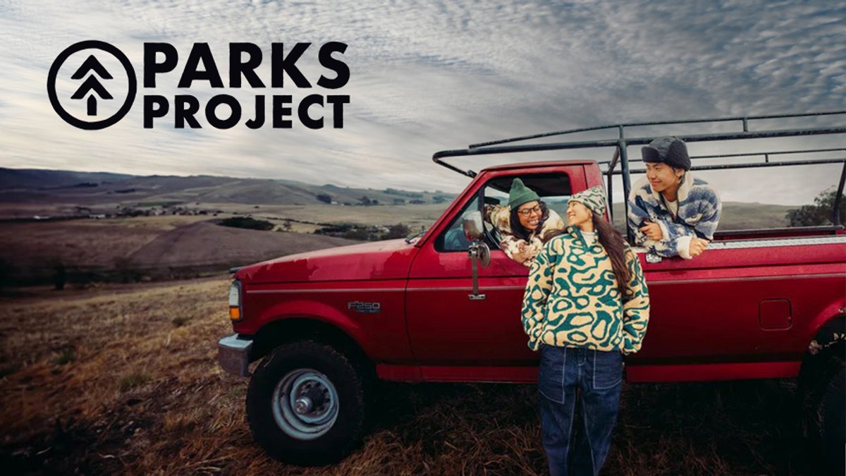 A family of four enjoys time together at a scenic overlook beside a red pickup truck in a sprawling countryside landscape.