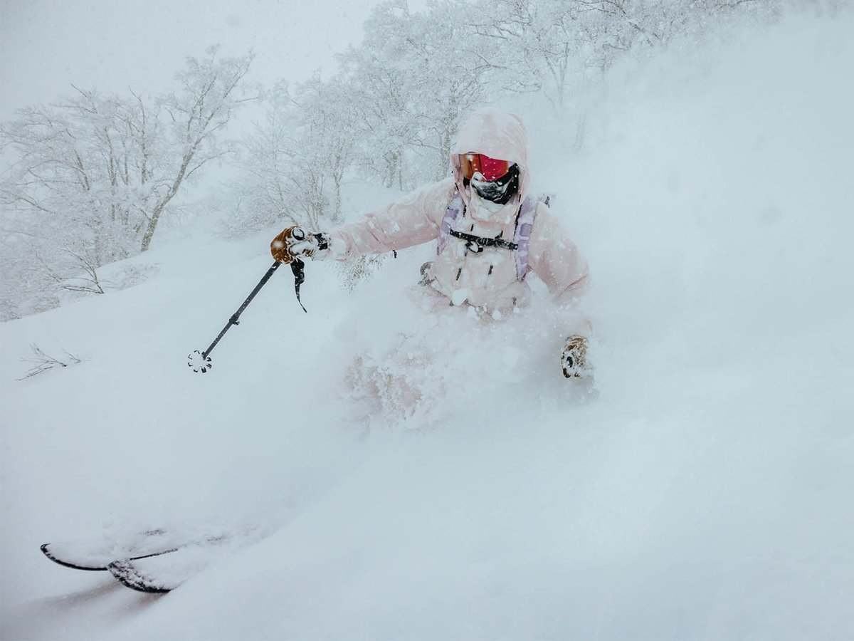 Skier making a turn in deep powder with top of pole and head visible over white snow cloud.