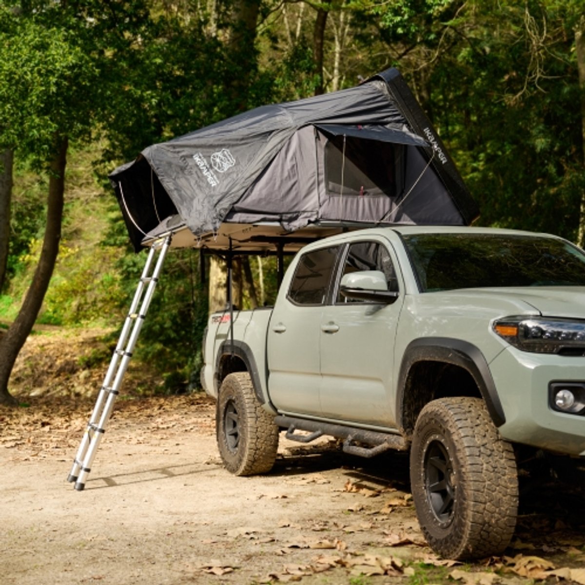 A pickup truck is positioned at a campsite with an open rooftop tent on its roof rack. 