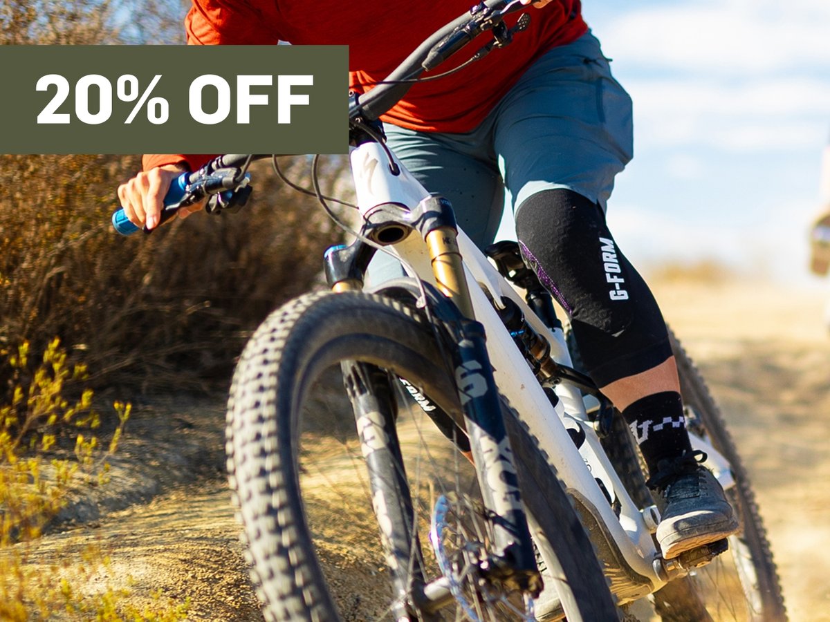 A man fixes his pads on a mountain bike.  A promotional flag says 20% off in the top right corner.