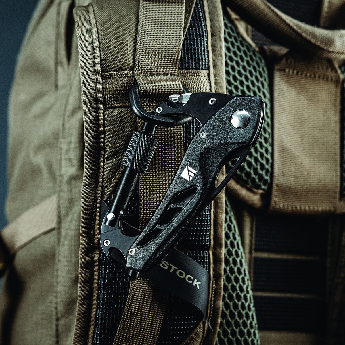 A black Dark Energy Carabiner Pro multi-tool clipped to the shoulder strap of a tan backpack.