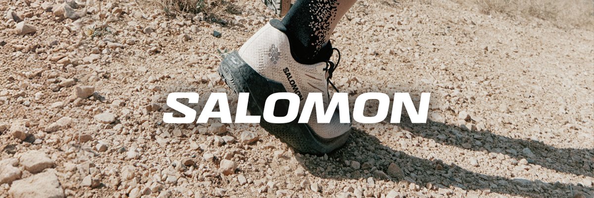 Salomon trail shoe mid-stride on a rocky desert dirt path, with patterned compression socks visible above.
