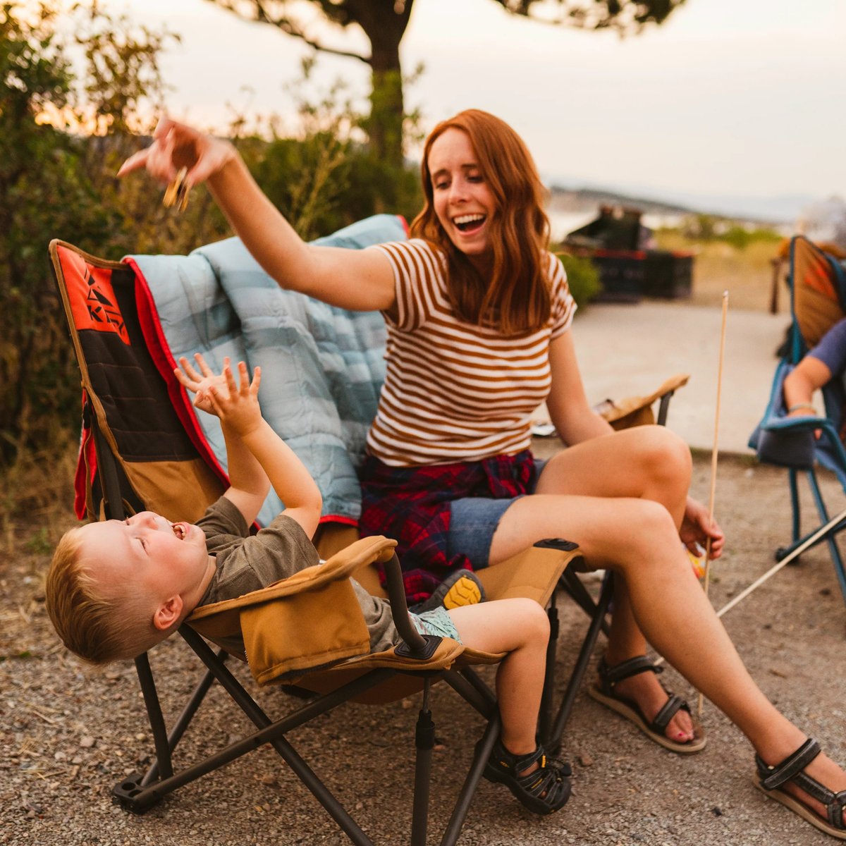 A group of people sit around a fire, with the focus on a man in a Kelty Low Loveseat camping chair.