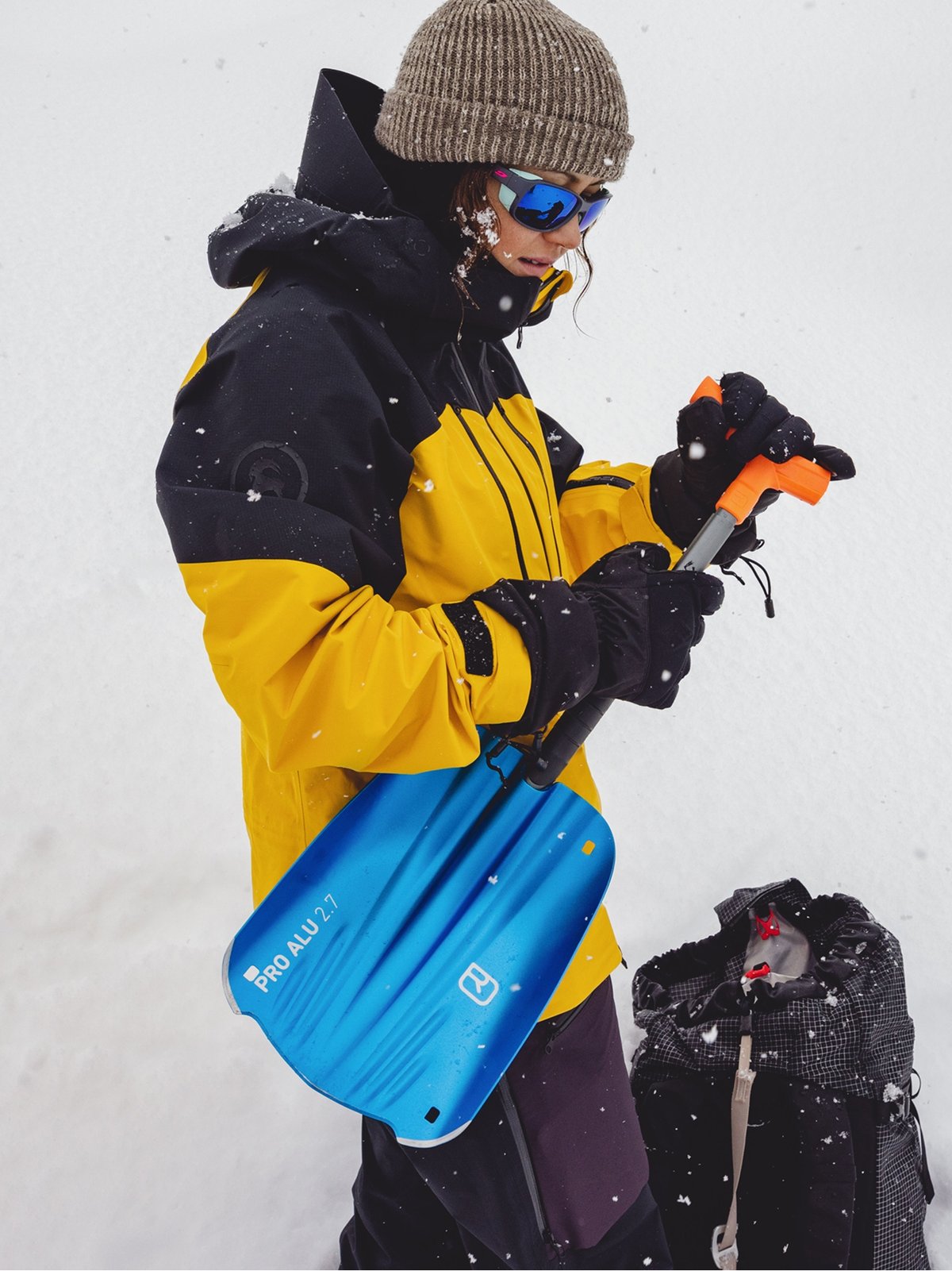 A woman wearing a yellow jacket holds a blue shovel.