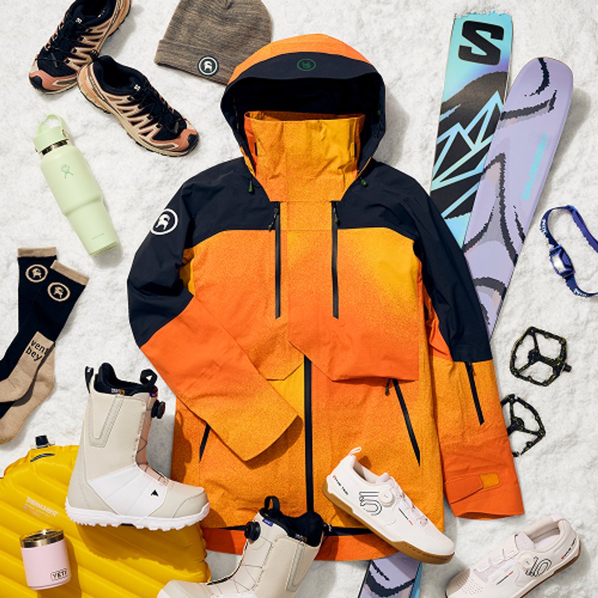 A flat lay display features an orange and ski jacket, a gray knit beanie, a pink Yeti tumbler, Burton  snowboard boots, Salomon skis, a headlamp, and the text: "25 more outdoorsy gift ideas."