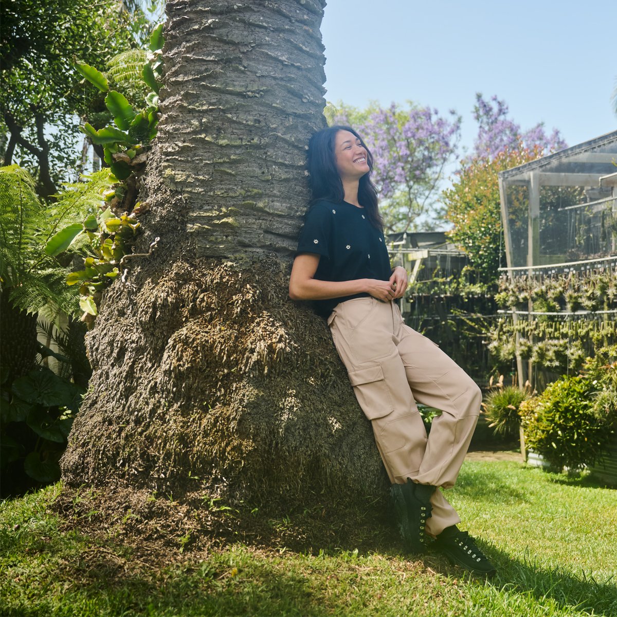 A woman leans against a tree as she wears the prAna Stretch Zion pants.