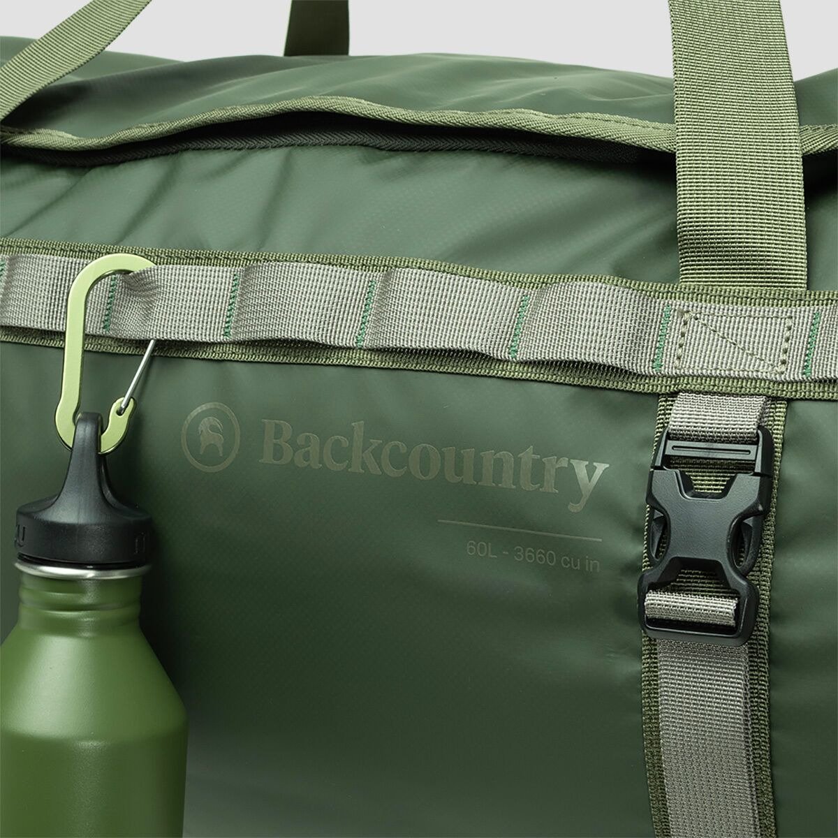 Close-up of a green duffel bag showing the fabric texture and a water bottle hanging from a carabiner on the external daisy-chain webbing.