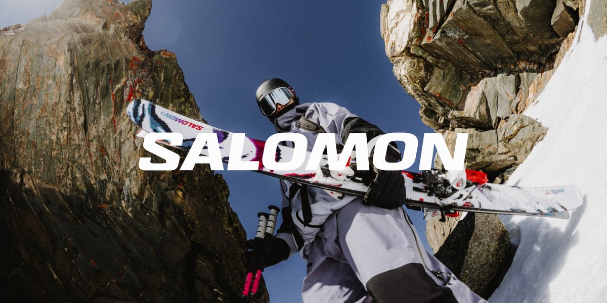 A skier walks between two large boulders. The word “Salomon” is over them.