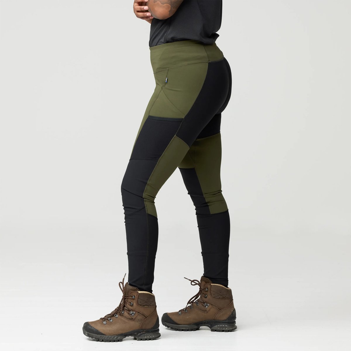 Women's olive green and black color-block hiking leggings with side pockets paired with brown hiking boots.