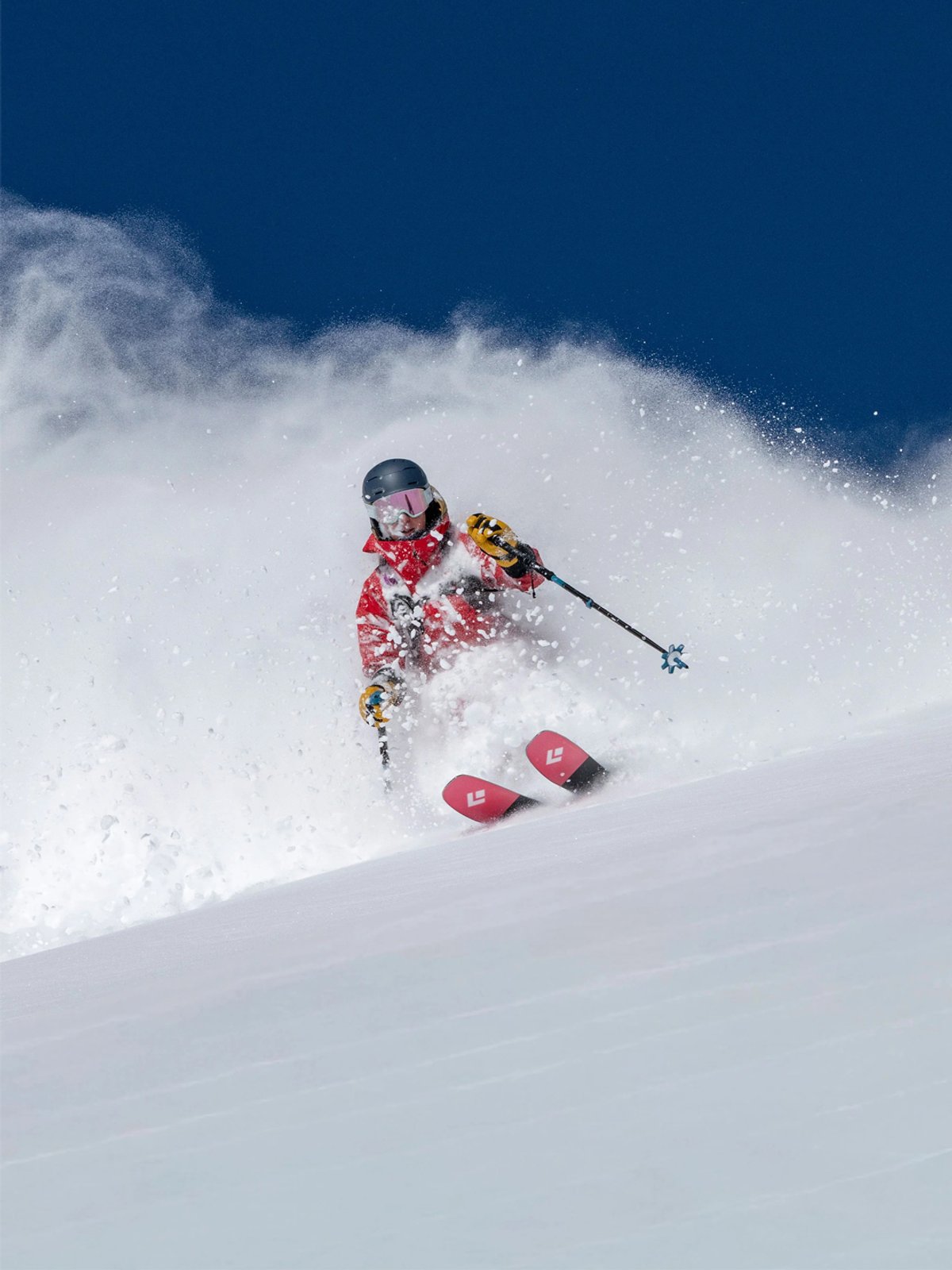 A person skis down a slope, powder spraying out behind tjem.