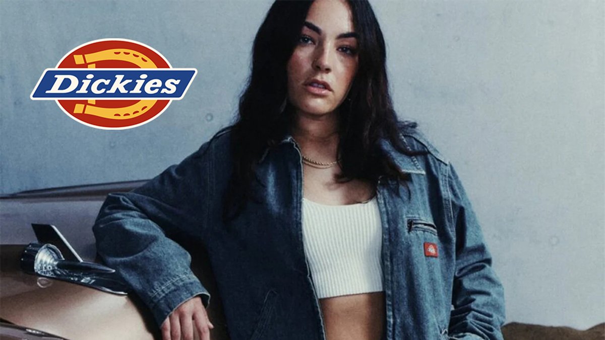 A woman wearing a denim jacket and white crop top leans against a vehicle in a casual outdoor setting with the Dickies logo displayed.