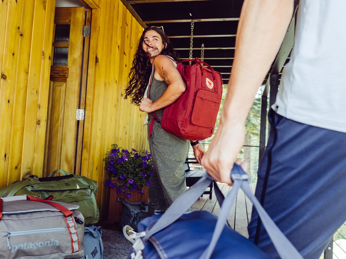 A pair of travelers carrying backpacks and suitcases in a tropical hotel lobby.