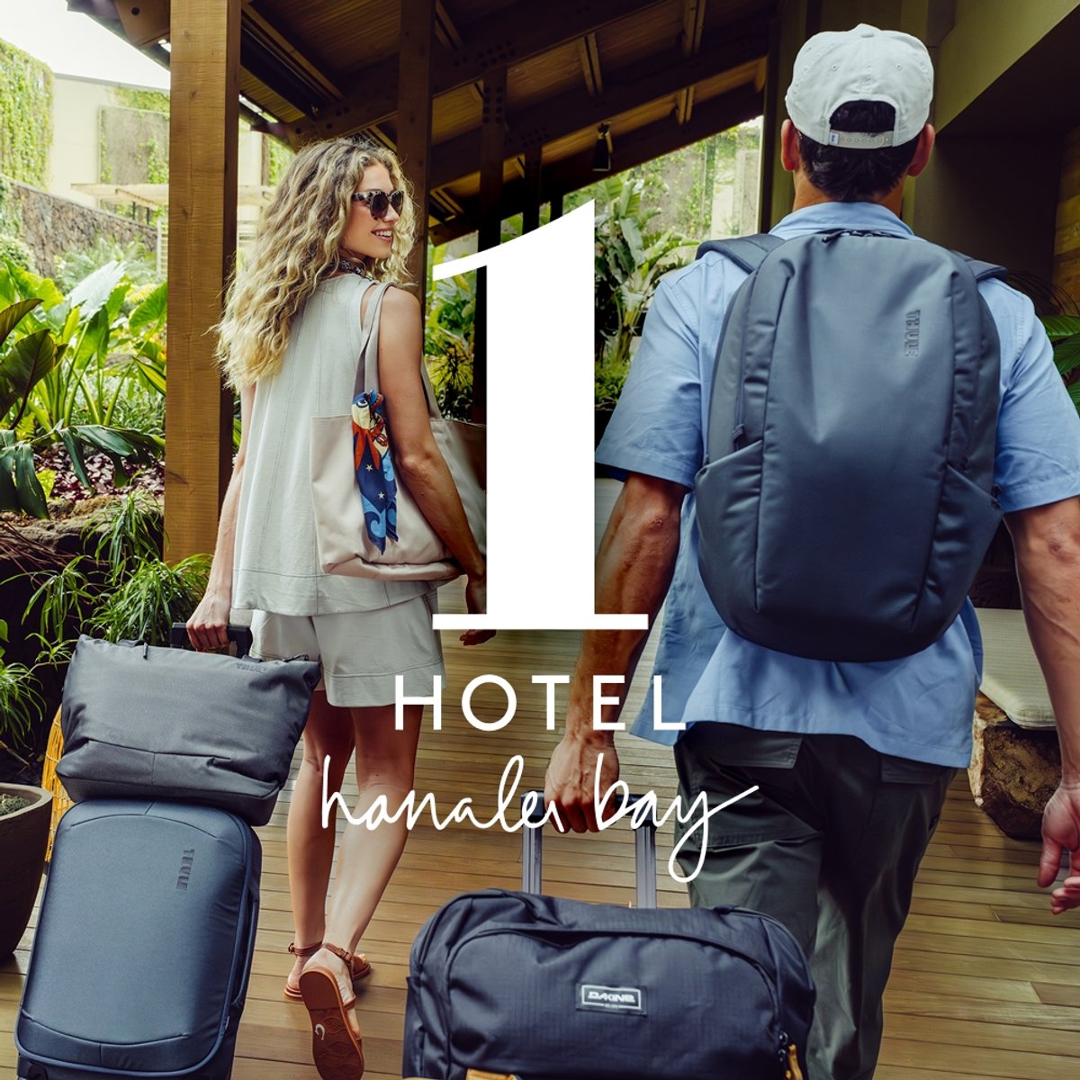 Two travelers arrive at 1 Hotel Hanalei Bay, rolling Thule luggage and wearing a Dakine backpack amid lush tropical greenery.