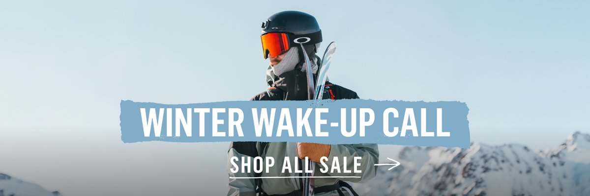 Skier in Oakley goggles and helmet holds skis on a snowy mountain peak. Text reads: Winter Wake-Up Call — Shop All Sale.