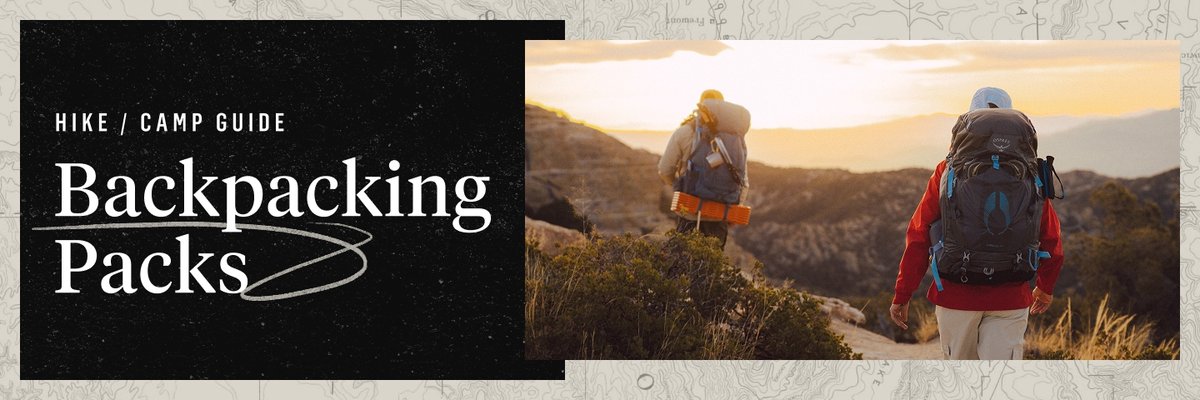 Two people carrying large backpacking packs walk towards the sunset setting over desert hills. The rocky trail winds between sand and desert shrubs. Words appear to the left of the hikers saying “Camp Guide, Backpacking Packs”.