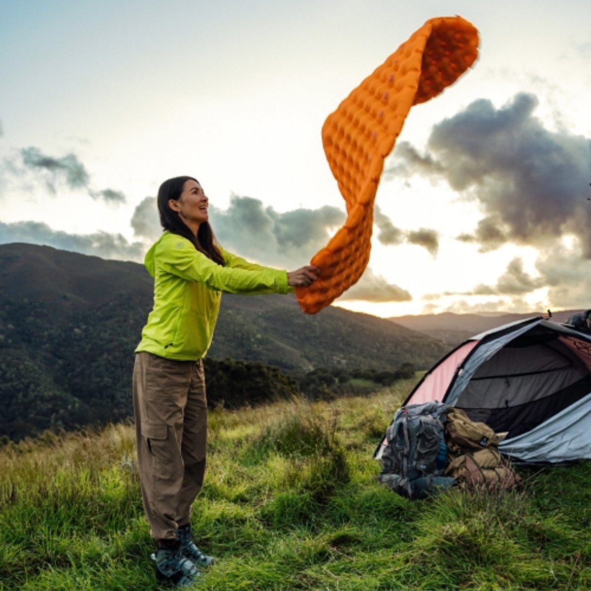 A camper fans out an orange sleeping pad at a scenic campsite. 