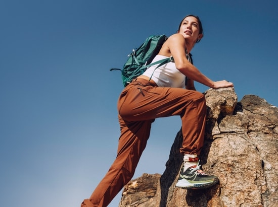 A woman in a tank top and hiking pants scrambles to a rocky summit.