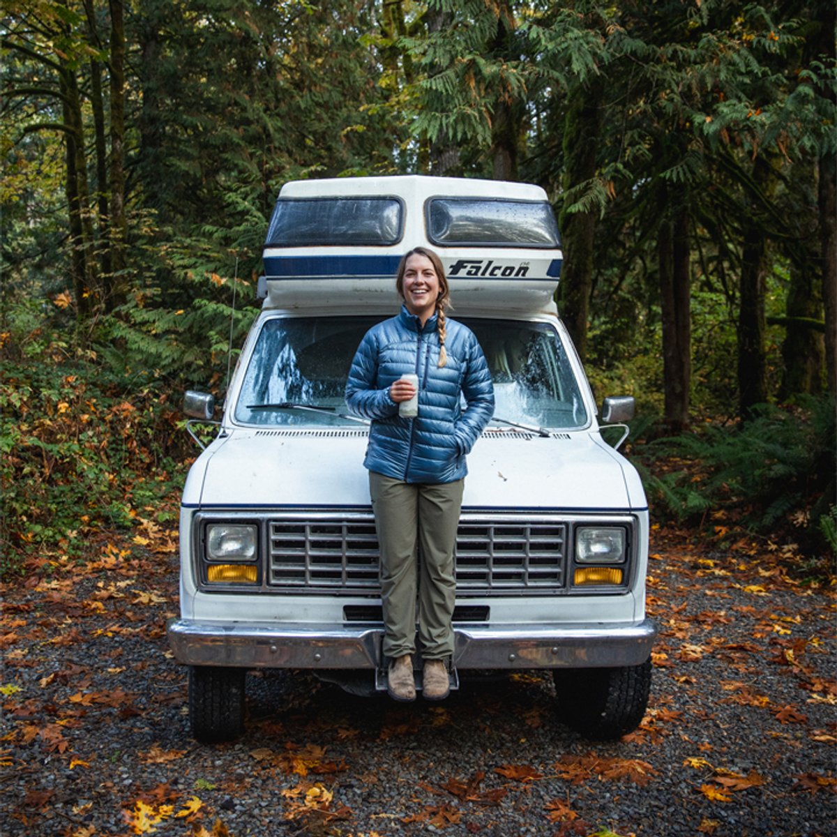 A woman wearing a Helium Down Jacket, leaning against the car. 